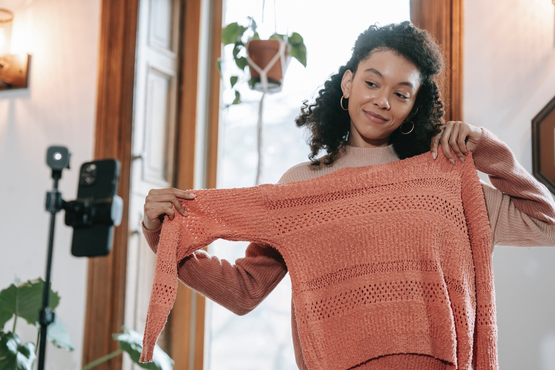 smiling ethnic woman trying on sweater and filming video