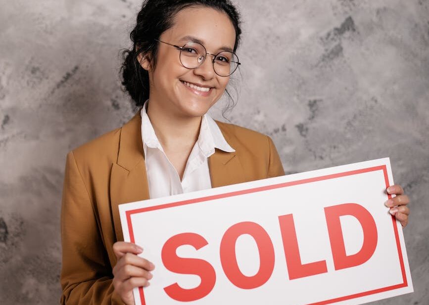 smiling woman holding a sold sign