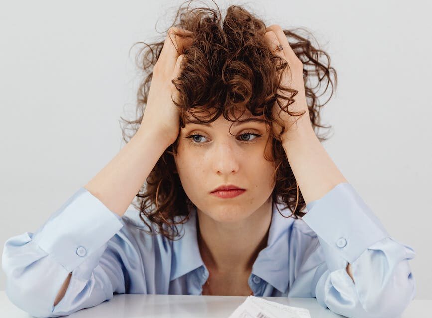 woman in blue long sleeve shirt holding her head
