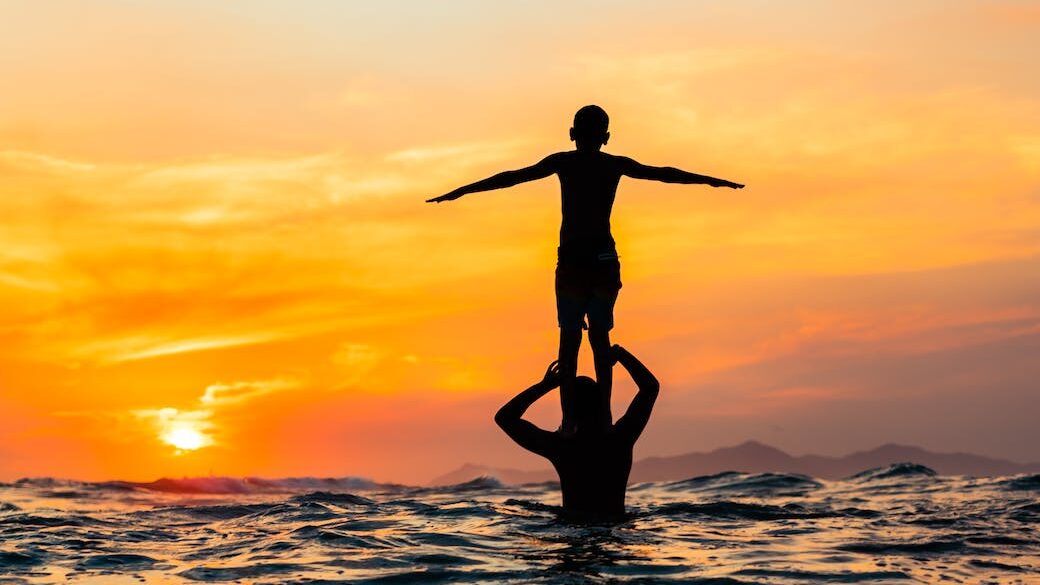silhouette of a child standing on the shoulders of a person while in the sea